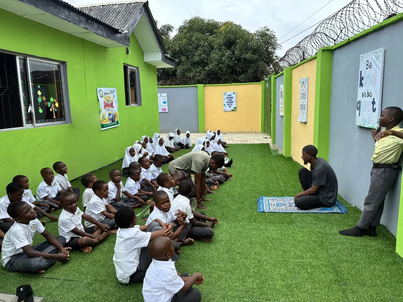 Pupils seated on the school lawn with their teachers after Salah